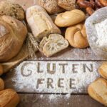 Gluten free sign in spiled flour with loaves of bread and ingredients around