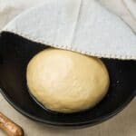 Bread dough in black bowl partially covered by cloth wipe