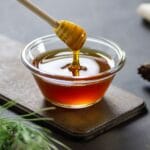 Glass bowl of honey with honey dipper on black table