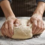 Kneaded dough by hands on table with spilled flour