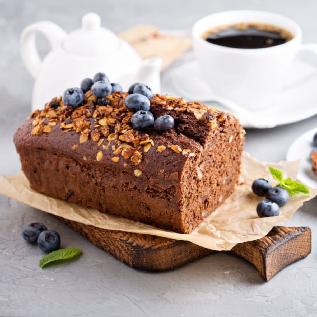 Loaf of bread with blueberries on wooden pad. Cup of coffe and pitcher in the background