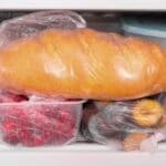 Loaf of bread in plastic bag on frozen fruits in freezer