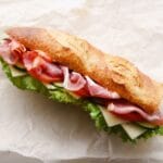 French baguette with salad, cheese, bacon on white paper sheet