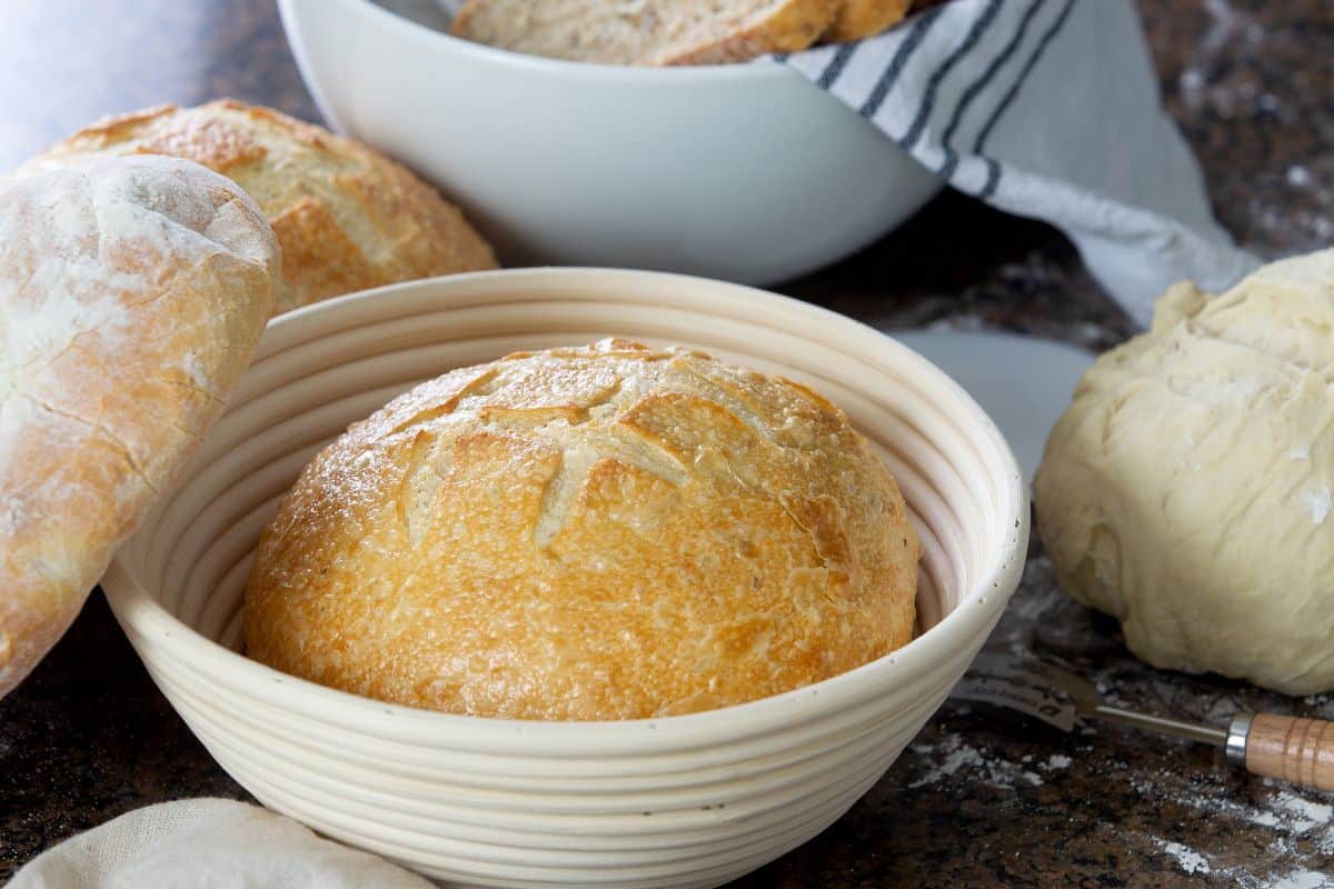 Loaf of bread in proofing basket next to loafs of bread, bread dough,