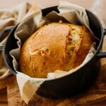 Black baking pot with load of bread on wooden pad
