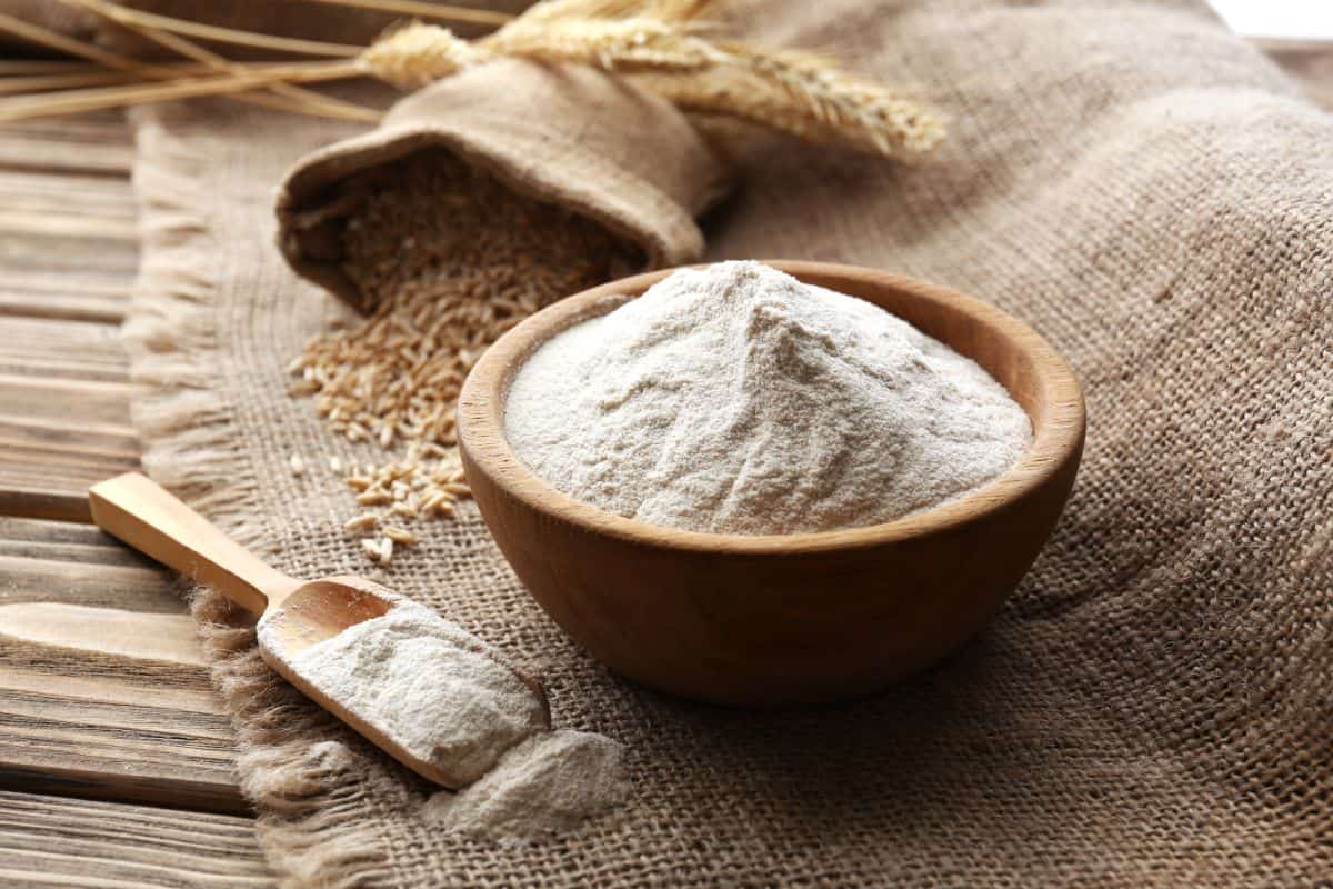 Flour in wooden bowl with spoon, sack of wheat grain, whole wheat, cloth bag on wooden table