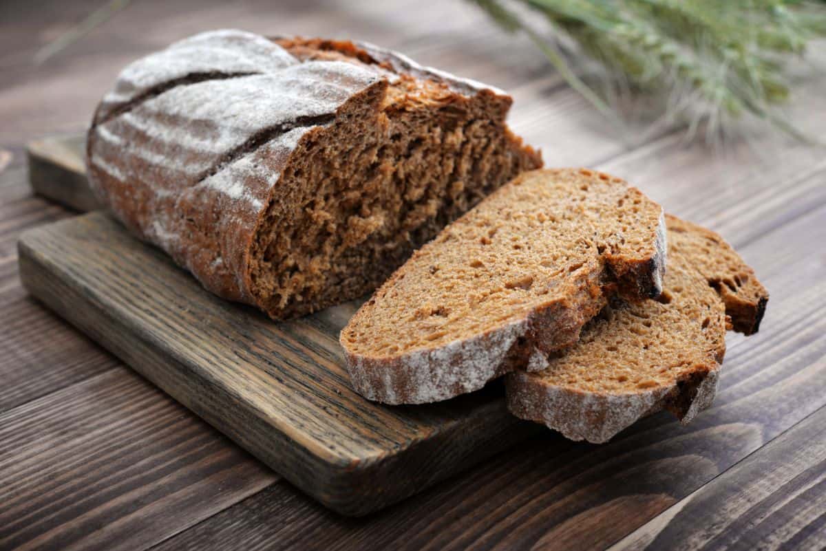 Loaf of bread partialy sliced on wooden pad on wooden table