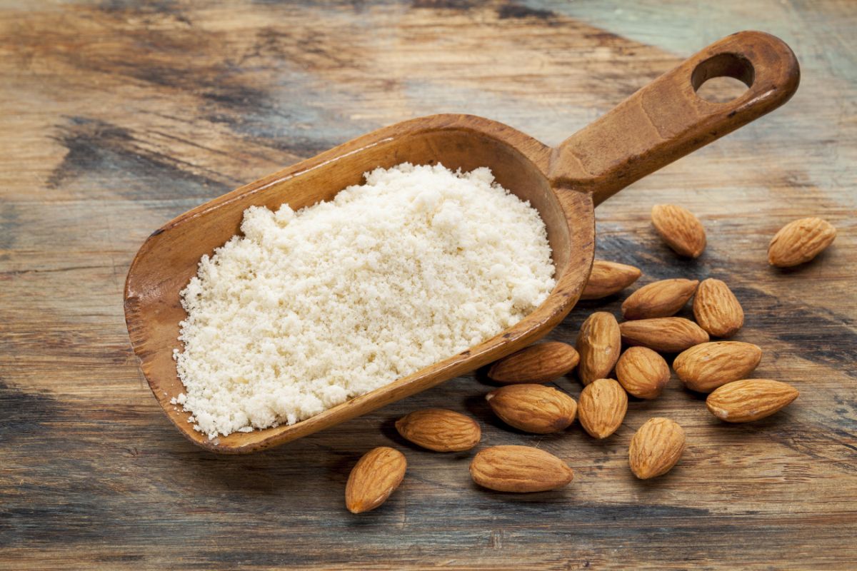 Wooden big spoon with almond flour on table with scattered almonds around