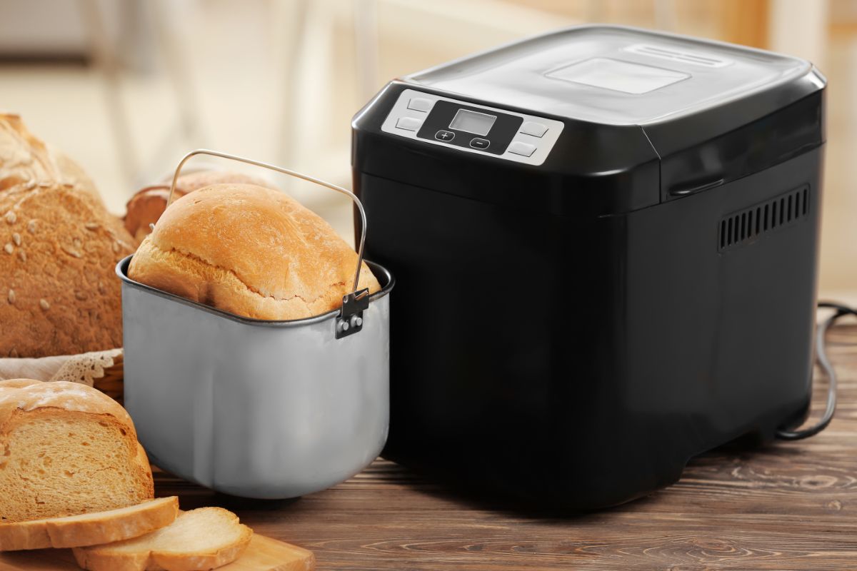 Black bread-maker machine with loaves of bread on wooden table