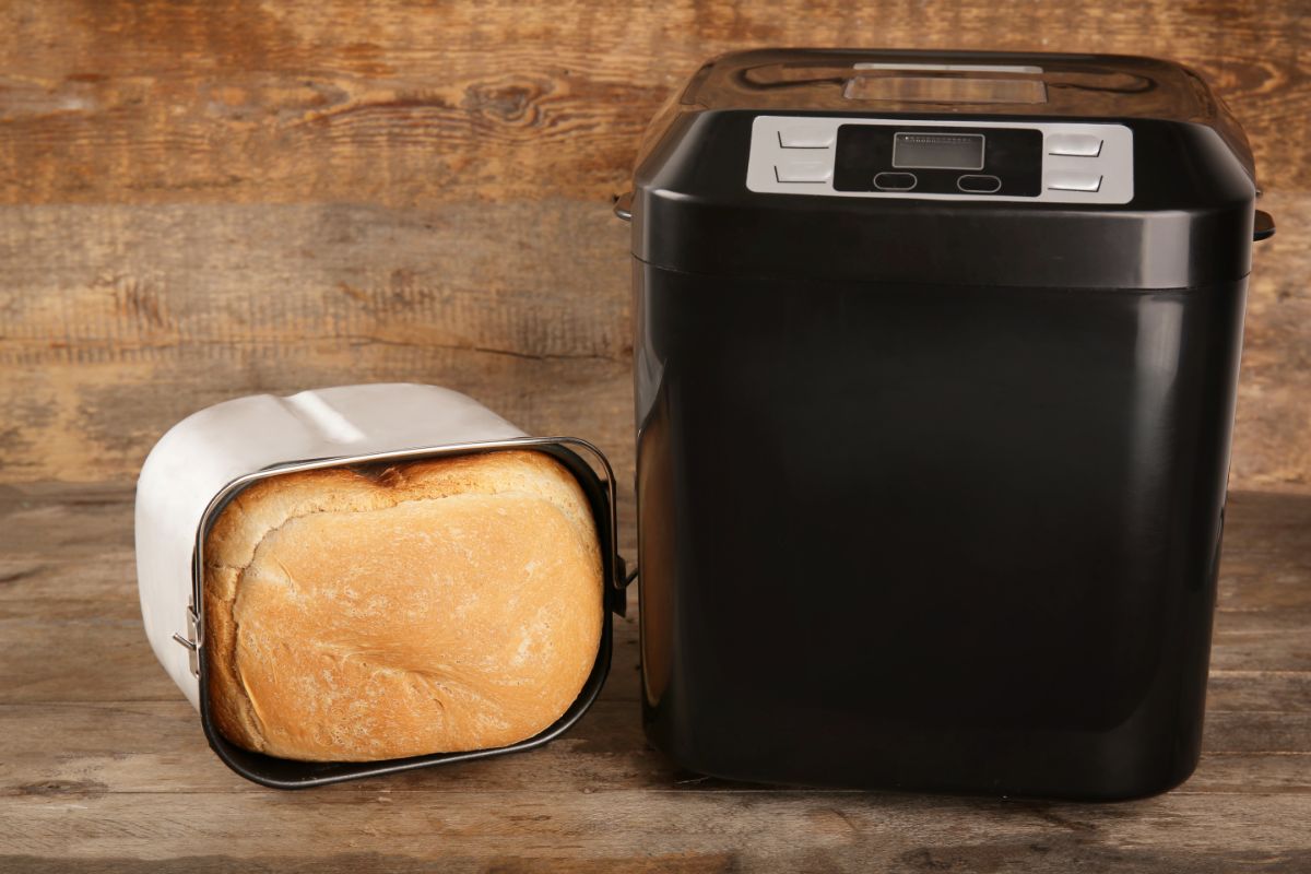 Black bread maker next to loaf of bread in mold on table