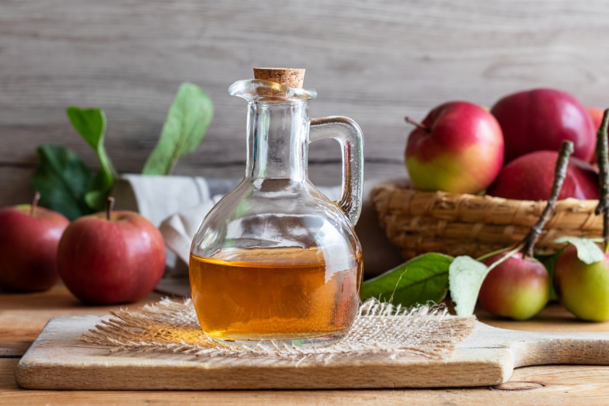 Apple vinegar in glass jar on wooden board, apples in the background