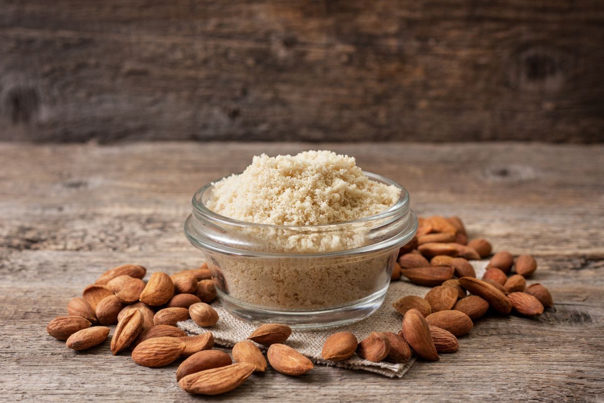 Glass bowl of almond flour on table with scattered almonds around