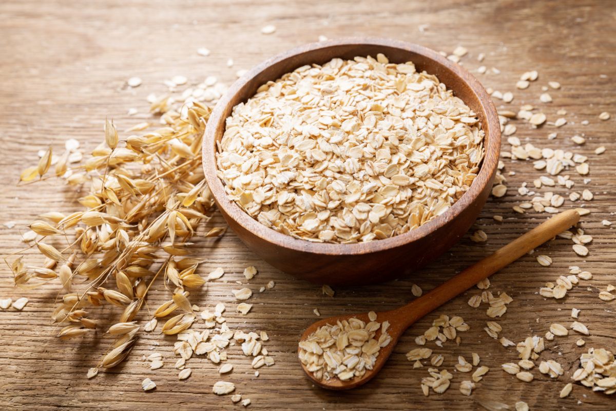 Wooden bowl full of oat flakes next to wooden spoon and oat 