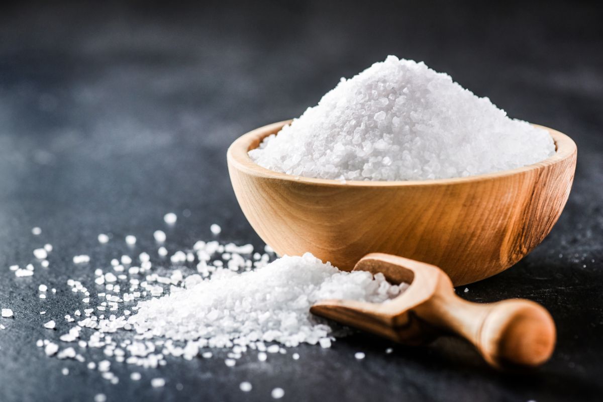 Wooden bowl of salt on black table with spilled salt and wooden spoon