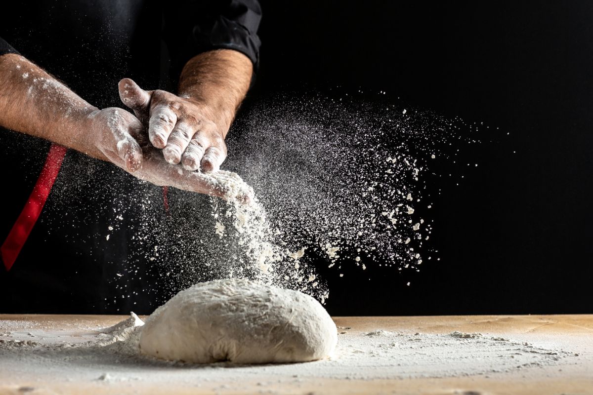 Chef dusting non baked loaf of bread with flour on wooden board