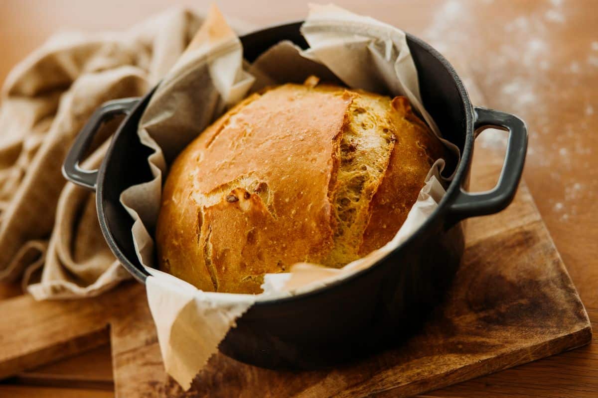 Black baking pot with loaf of bread on wooden pad