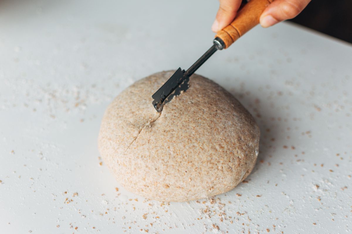 Bread dough being scored by knife held by hand  on white board