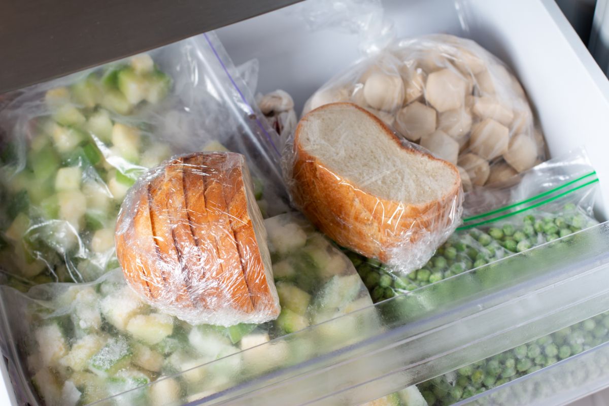 Sliced bread in plastic bags on freezer shelf full of frozen vegetable