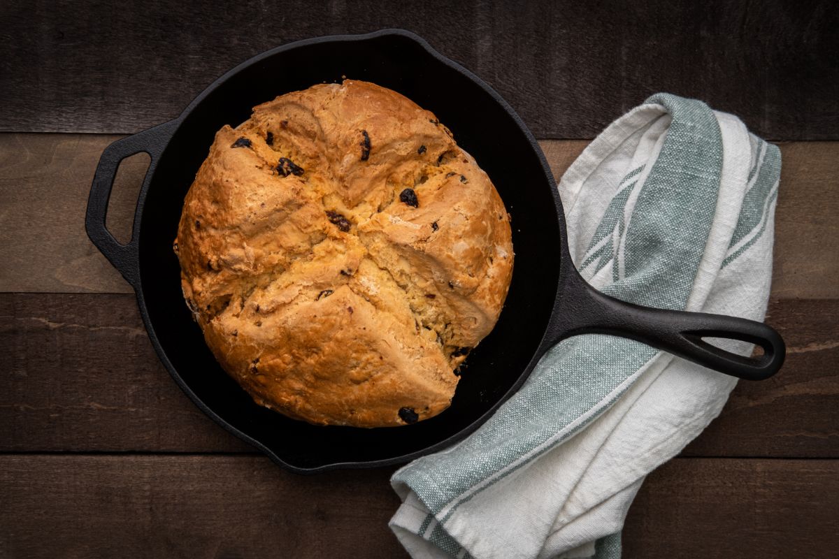 Loaf of bread in black pan next to cloth wipe on wooden table