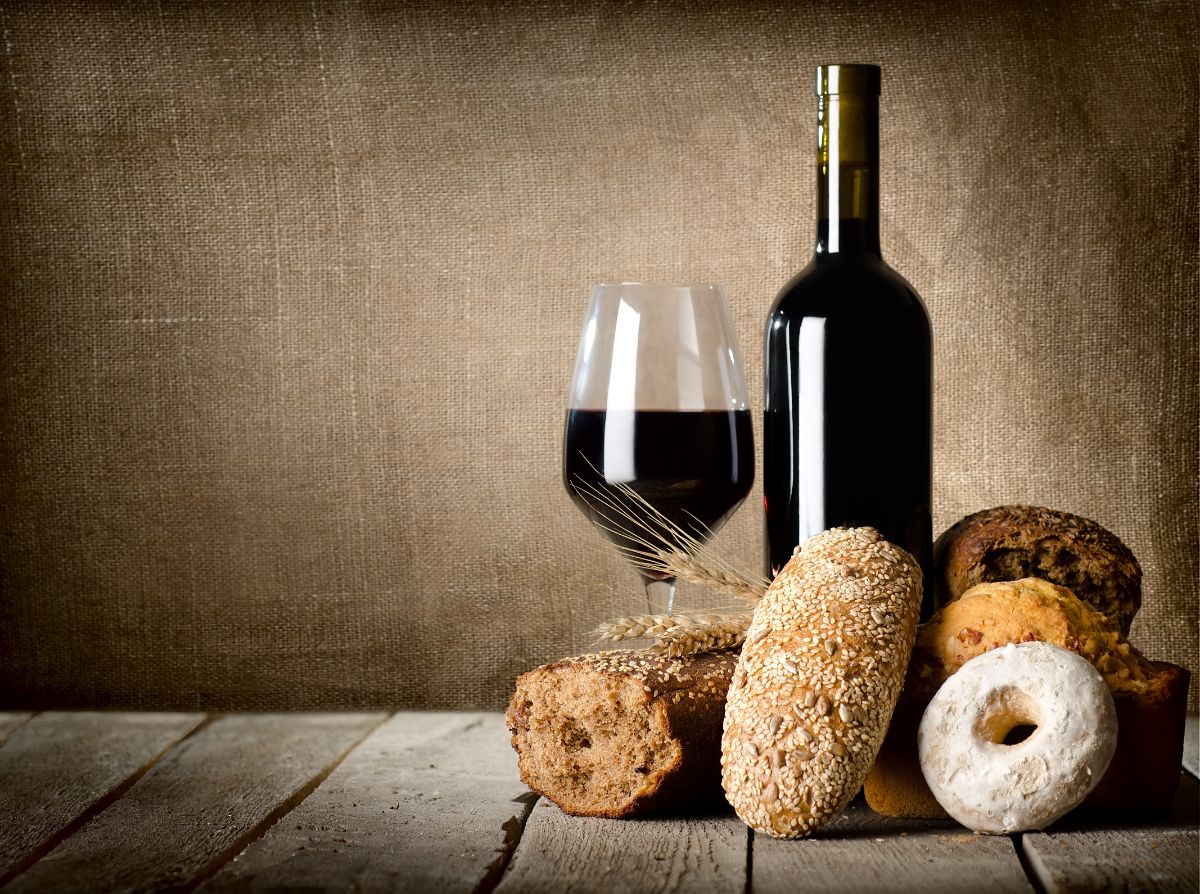 Different types of bread, glass and bottle of wine on wooden table