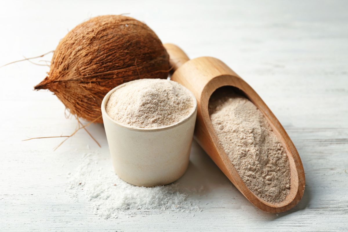 White cup and wooden spoon full of coconut flour on table with coconut