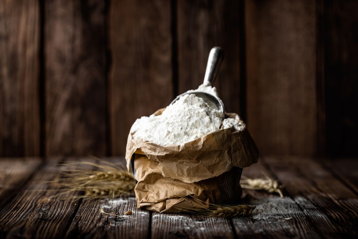 Flour with spoon in paper bag on wooden table