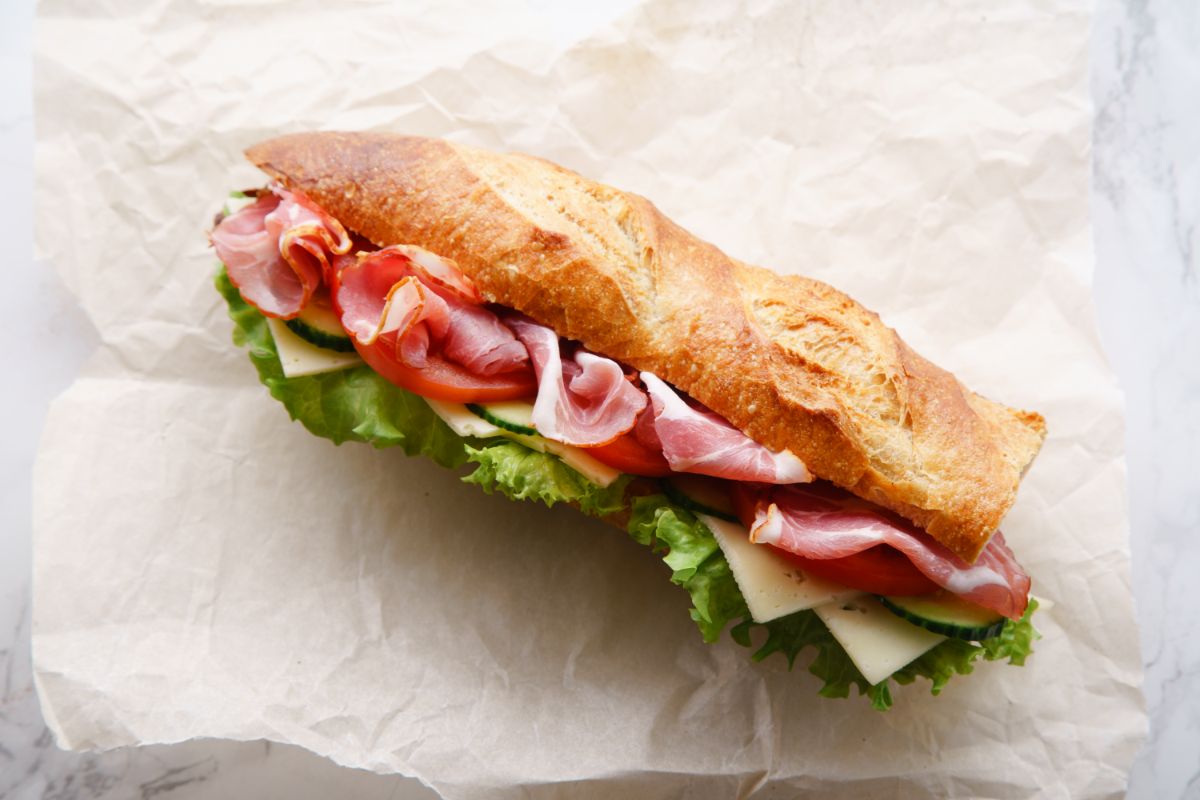 French baguette with salad, bacon and cheese on white paper sheet