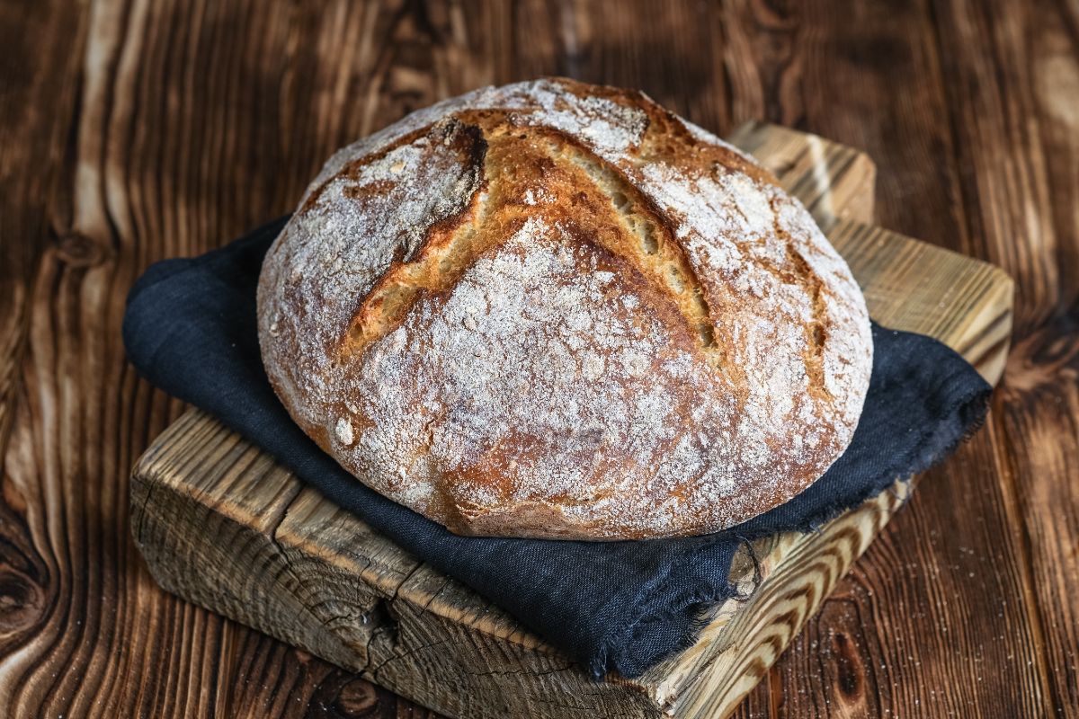 Freshly baked loaf of sourdough bread on wooden pad with cloth wipe