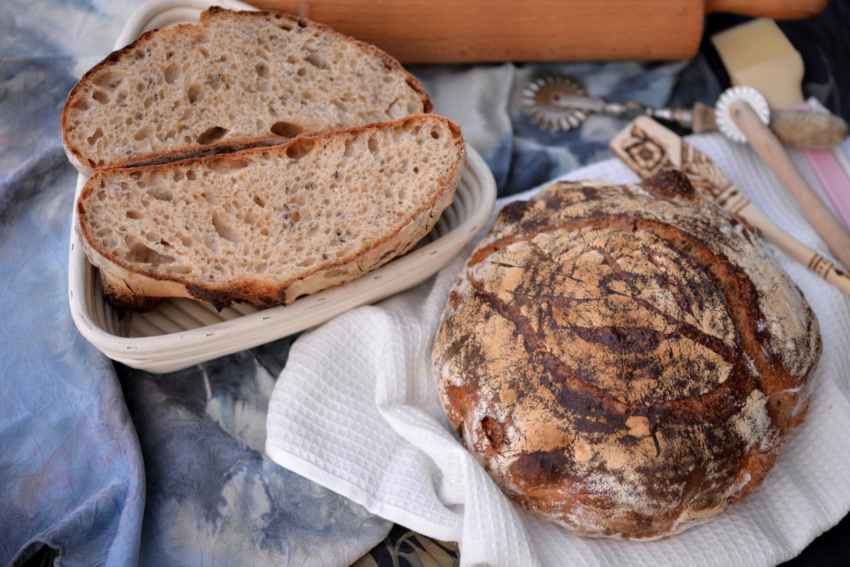 Loaf of bread, slices of bread, wooden kitchen roller, kitchen tools on table