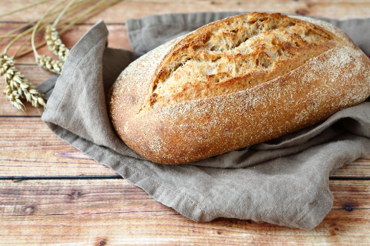 Freshly baked loaf of bread on cloth wipe on wooden table with wheat