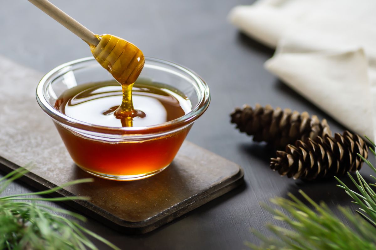 Glass bowl of honey with honey dipper on wooden pad on black table