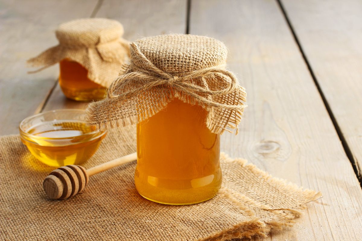 Glass jars of honey with bowl of honey and honey dipper on wooden table with cloth