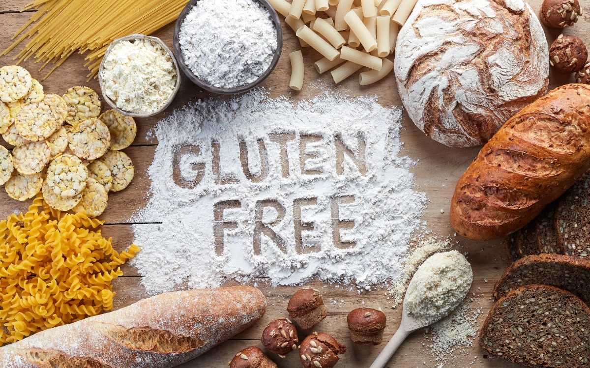 Gluten free sign in spilled flour on table with loaves of bread and ingredients around
