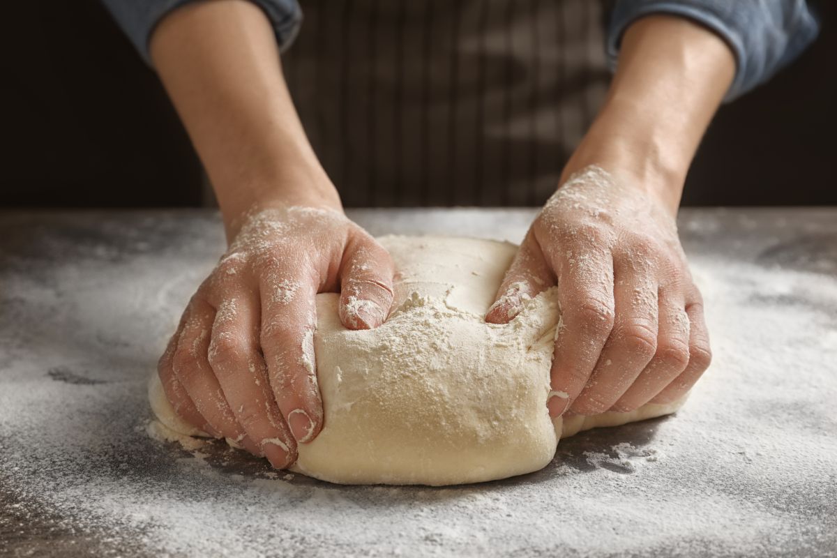 Dough being kneaded by hands on table with spilled flour