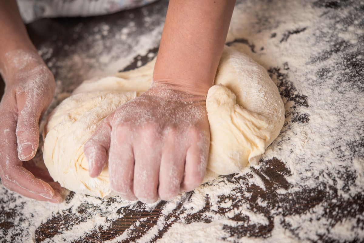 Dough being kneaded by hands on table with spilled flour