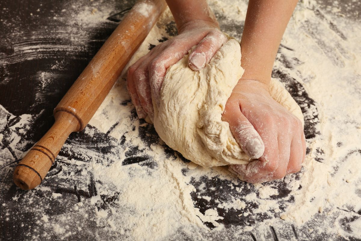 Hands kneading dough on flour dusted board with wooden kitchen roller