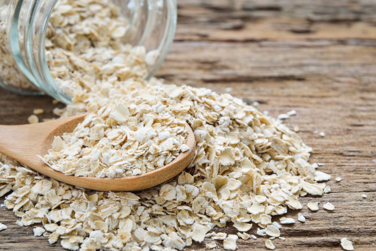 Spilled oat flakes from glass jar on wooden spoon and table