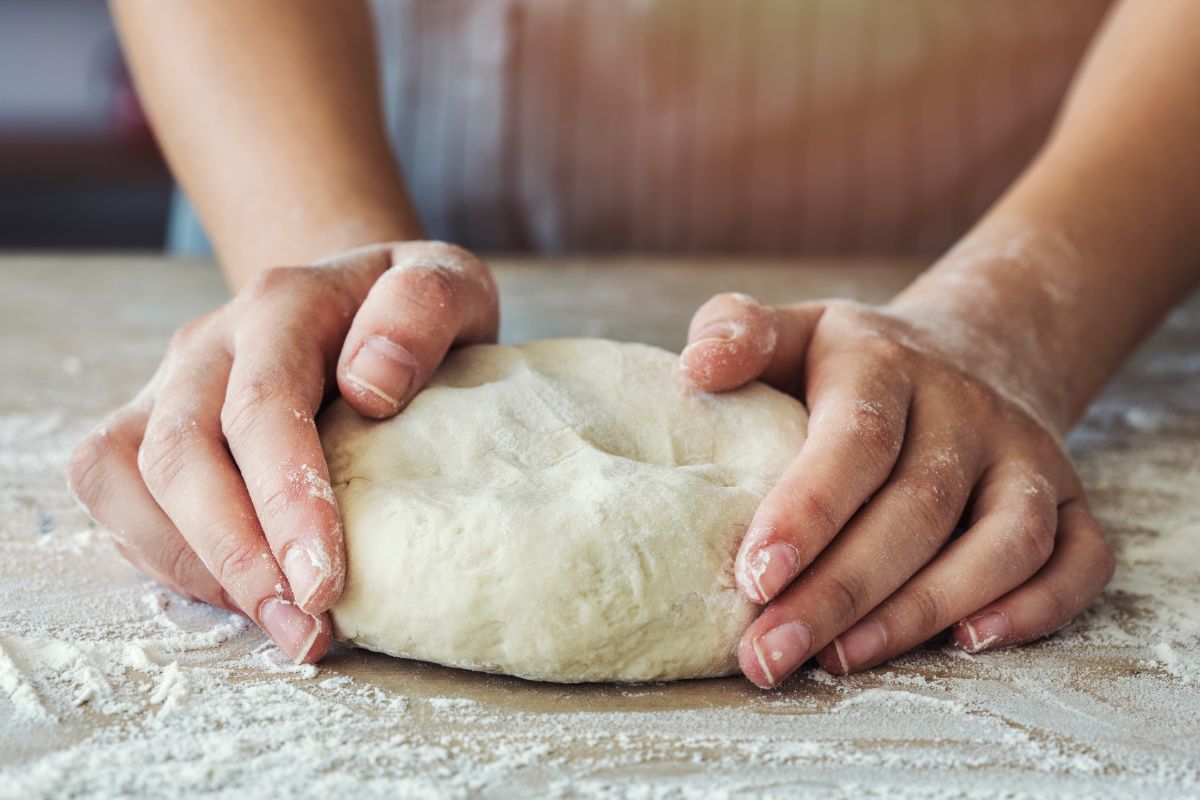 Dough on flour dusted board being kneaded by hands