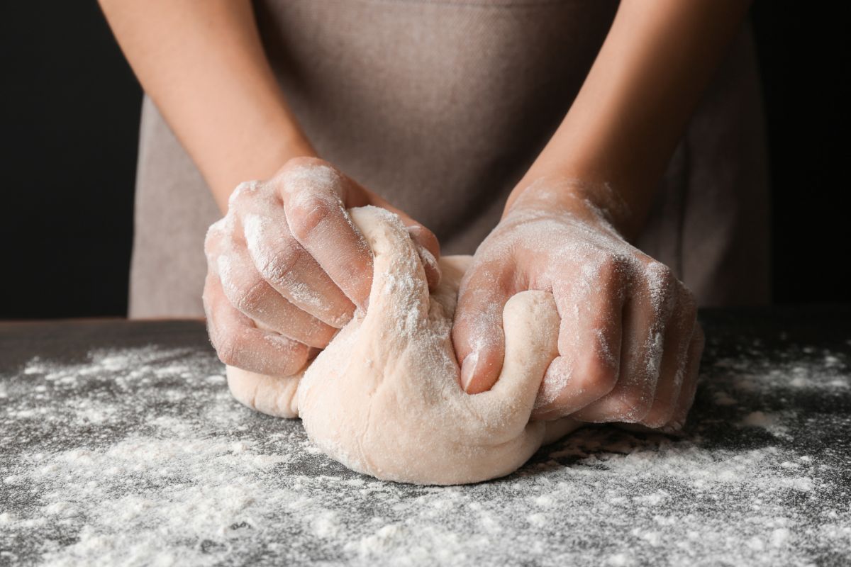 Dough on black flour dusted board being kneaded by hands