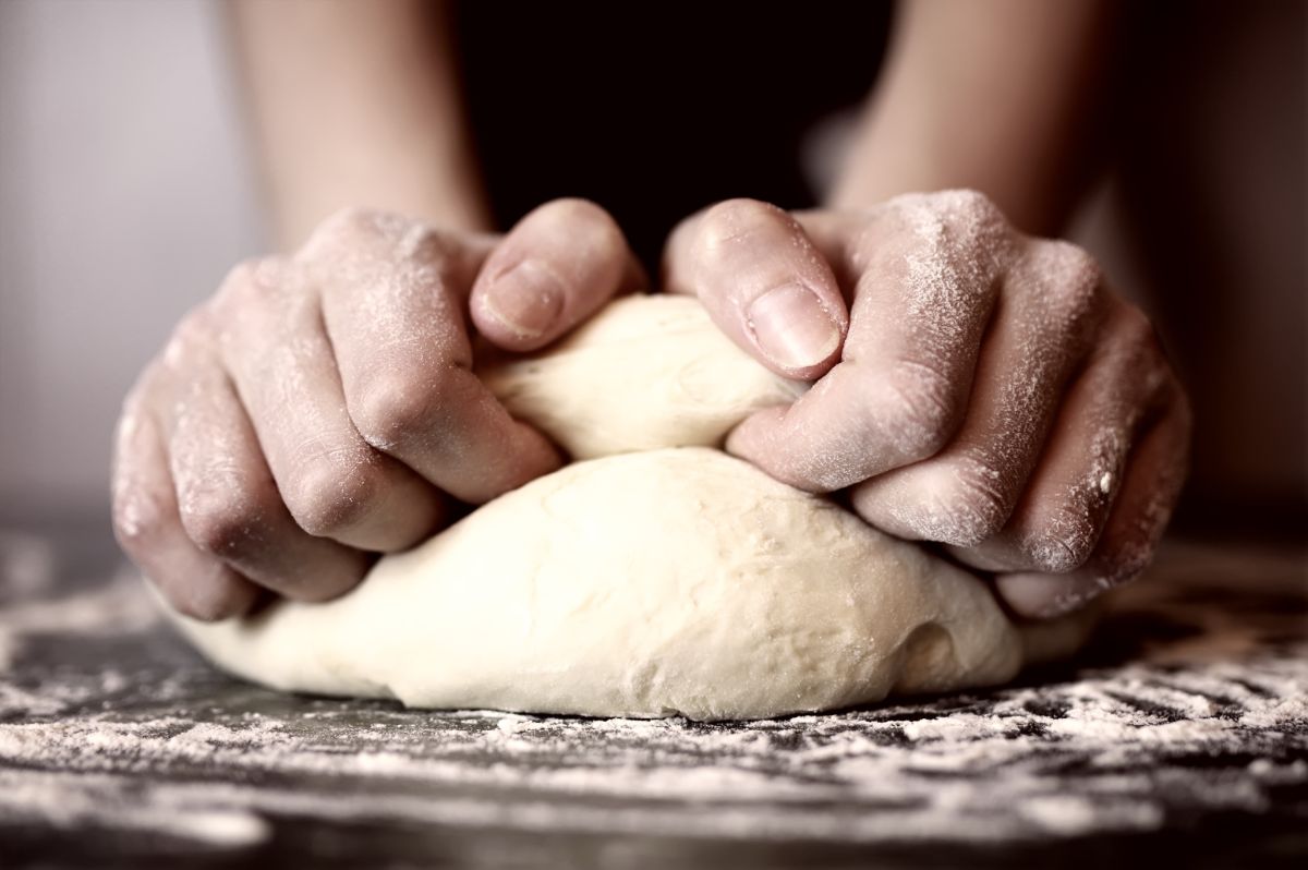 Pizza dough kneaded by hands on table with spilled flour