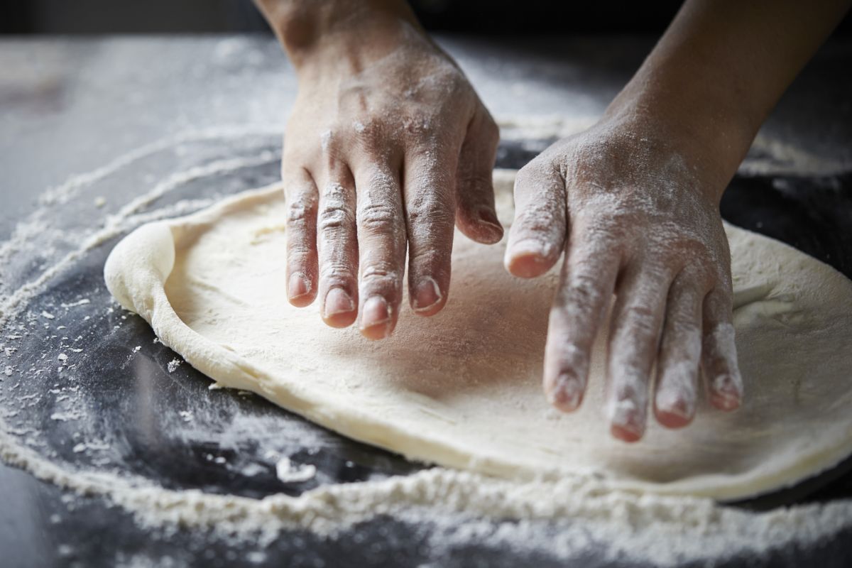 Pizza dough with hands over on black table with spilled flour