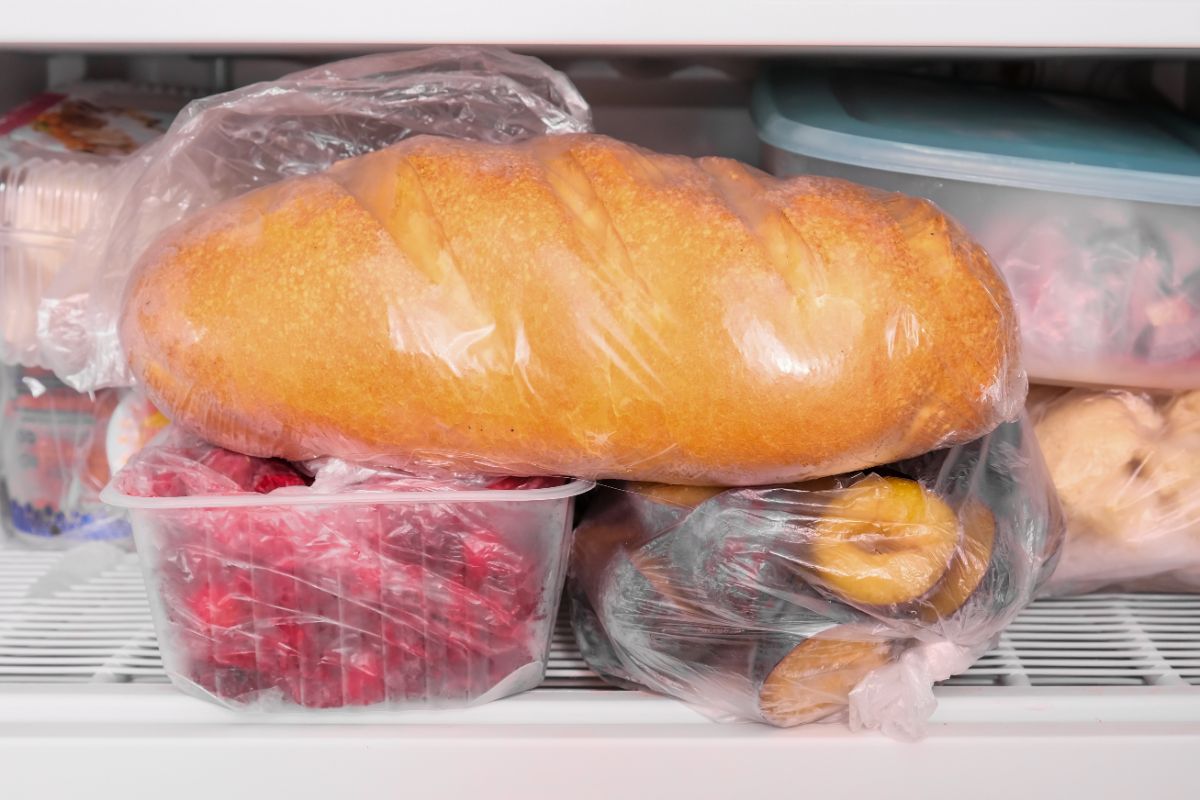 Loaf of bread in plastic bag on frozen fruits in freezer