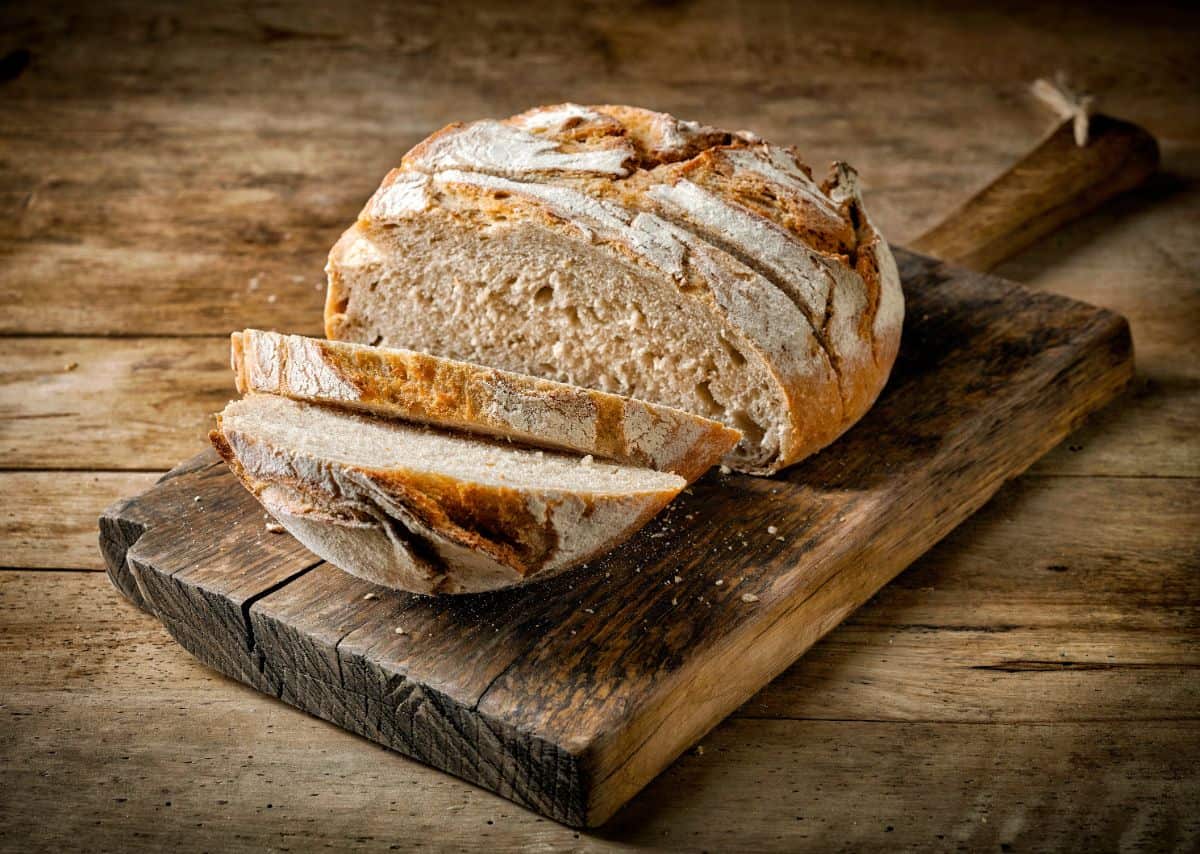 Homemade partialy sliced loaf of bread on wooden pad