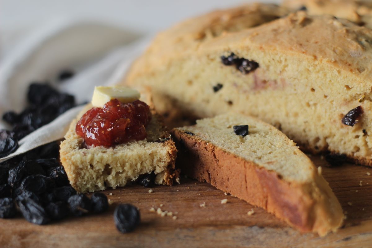 Slices of quick irish bread with jam, butter, and fruits on wooden board