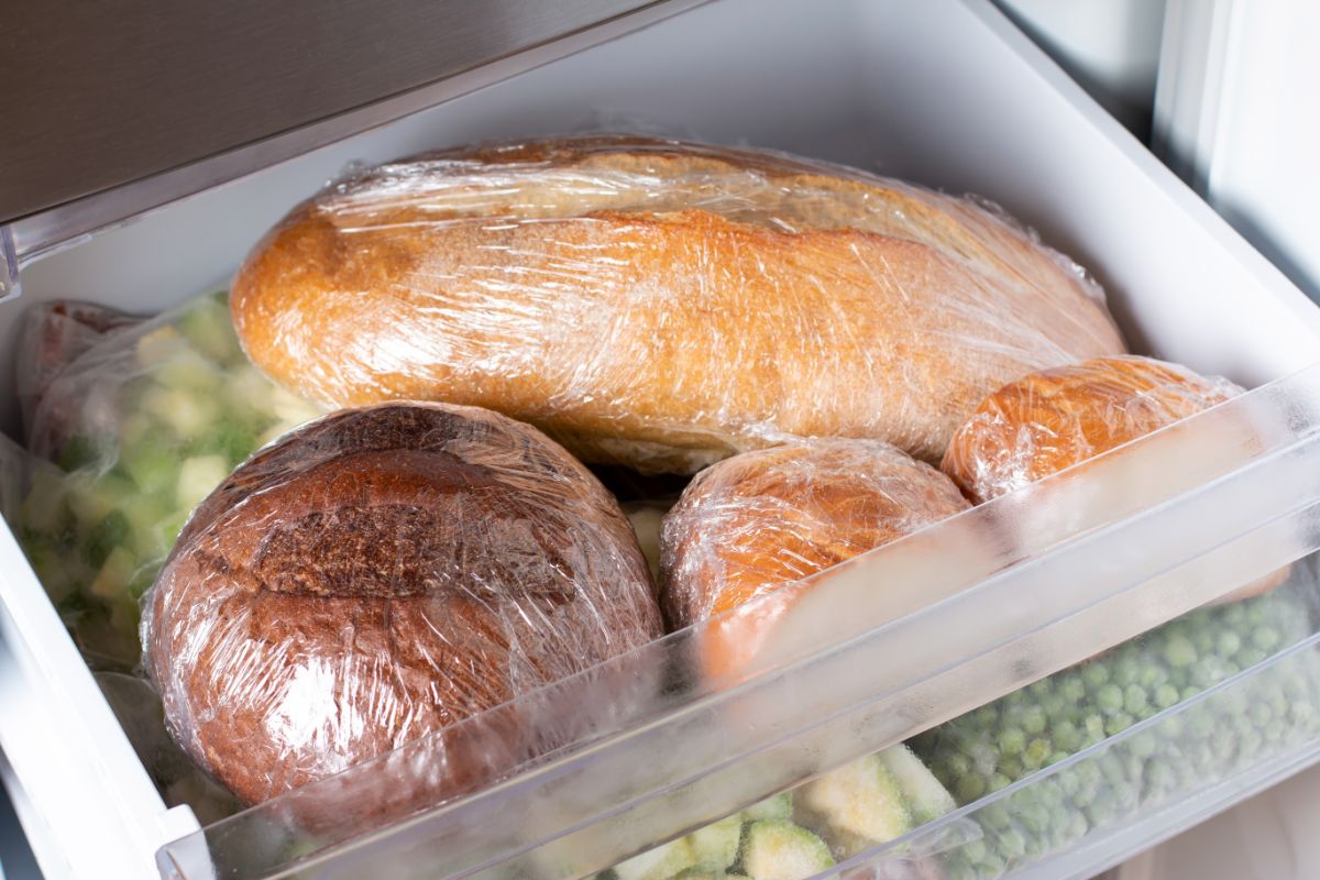 Loaves of bread in plastic bags in freezer shelf with vegetable