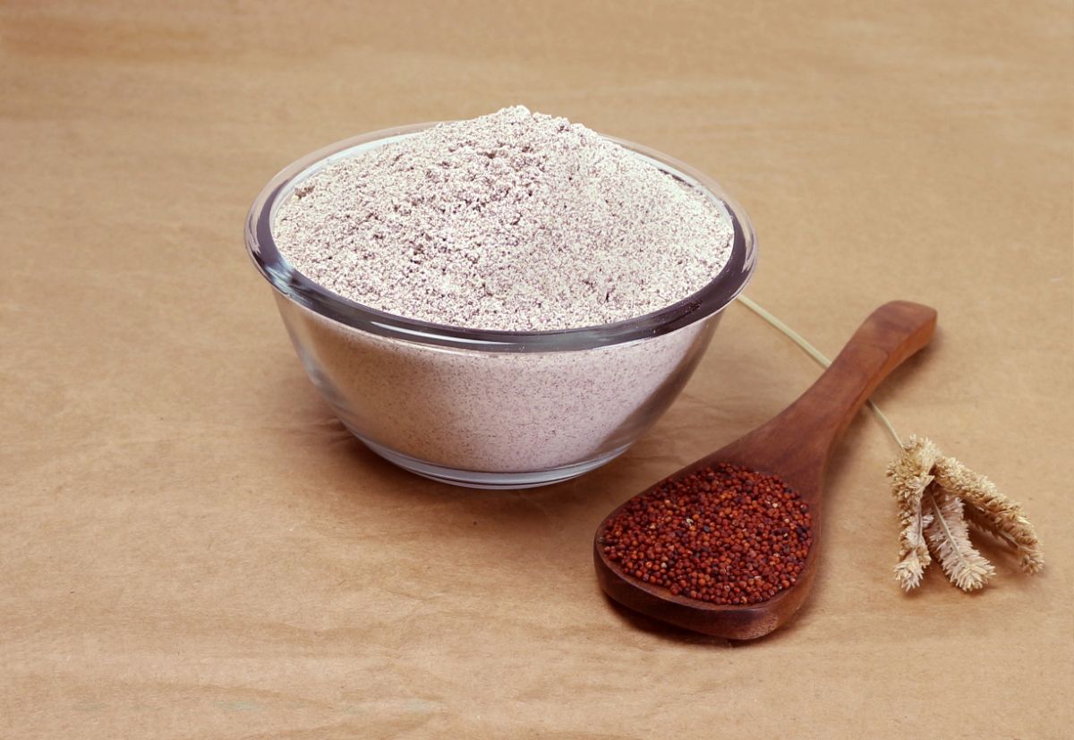 Millet flour in glass bowl and millet on wooden spoon on brown table