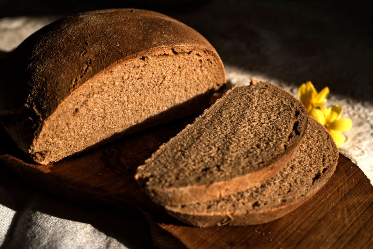 Partially sliced homemade loaf of bread on wooden cutting board