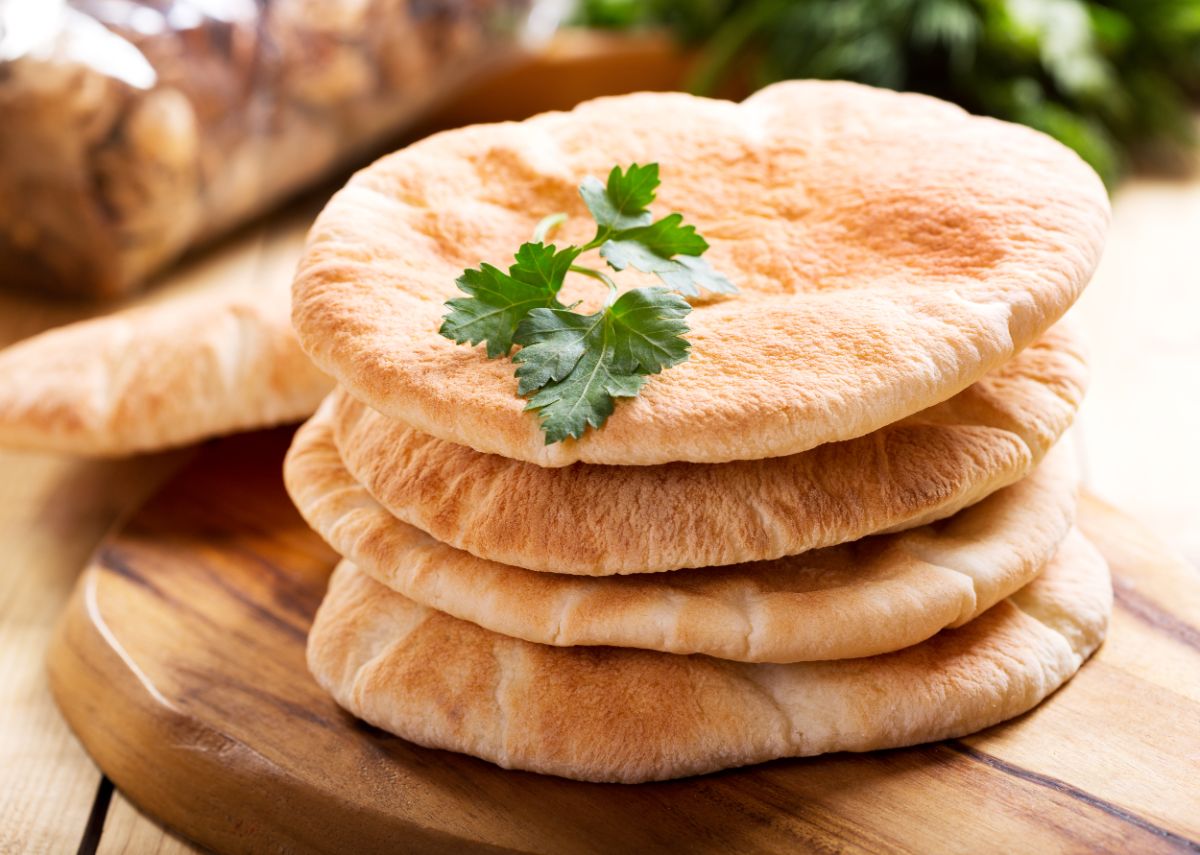 Pile of pita bread on wooden board with herb on the  top