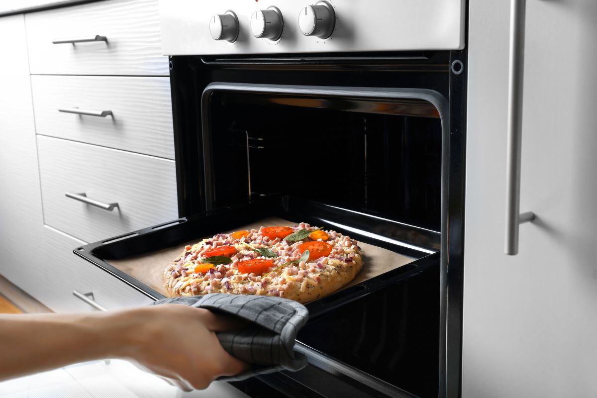 Hand held baking sheet with pizza being put in oven