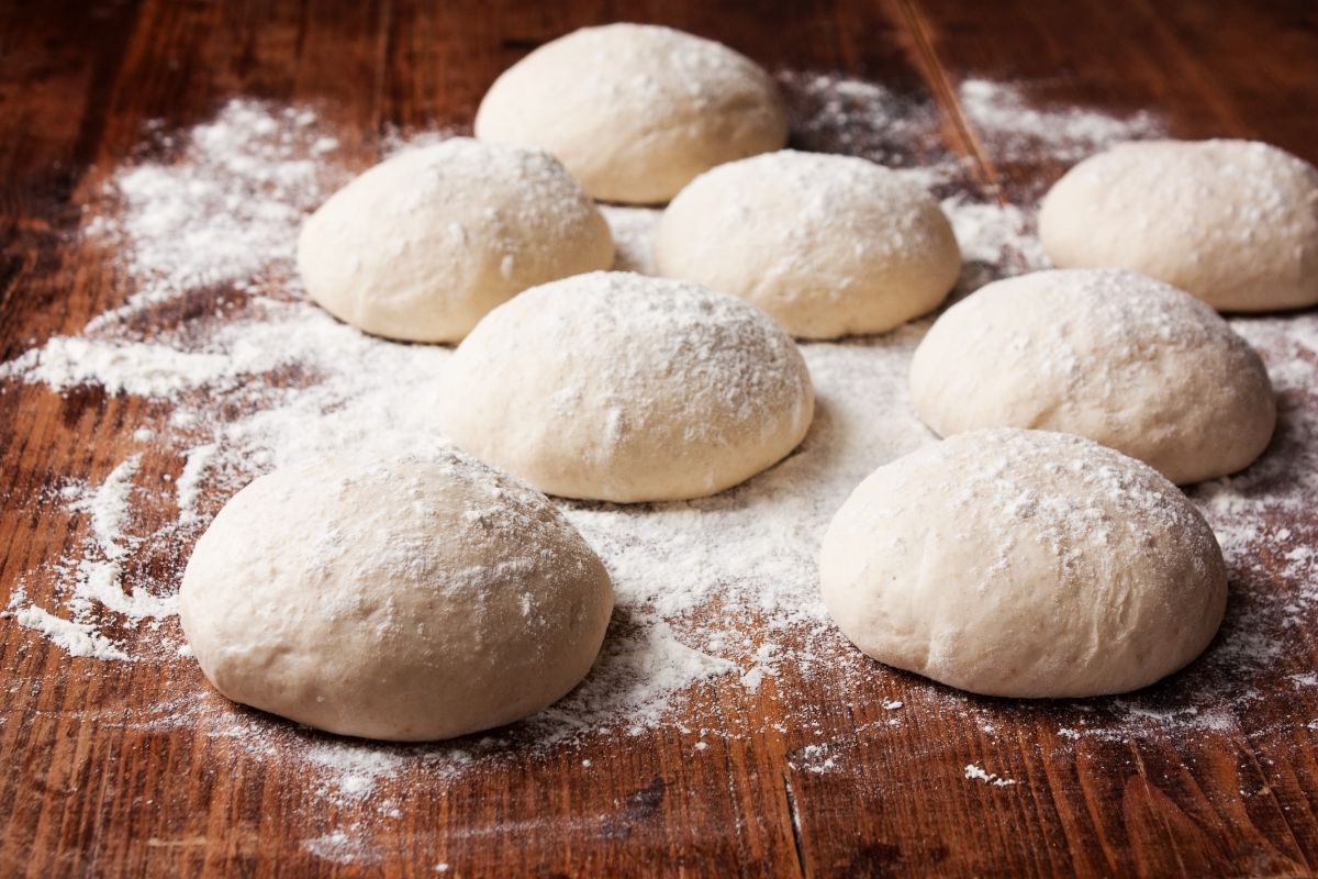 Pizza dough with spilled flour on a wooden table